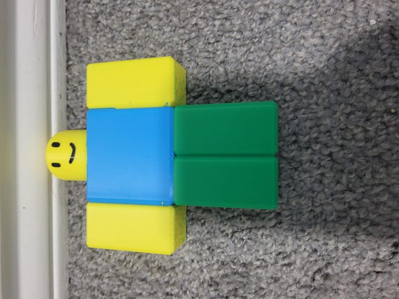 May include: A colorful toy figure with a yellow head and legs, a blue torso, and green arms. The figure has a smiling face. The toy is designed in a blocky style, reminiscent of a popular video game character.