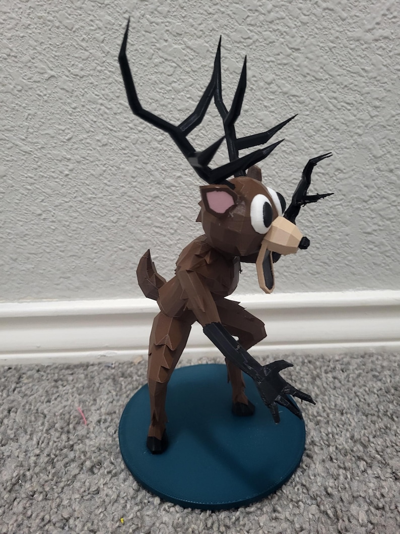 K&ouml;nnte beinhalten: Eine braune, geometrische Hirschfigur mit gro&szlig;en schwarzen Geweihen und schwarzen Krallen. Der Hirsch steht auf einem kreisf&ouml;rmigen Sockel in T&uuml;rkis. Die Augen des Hirsches sind gro&szlig; und wei&szlig; mit schwarzen Pupillen.