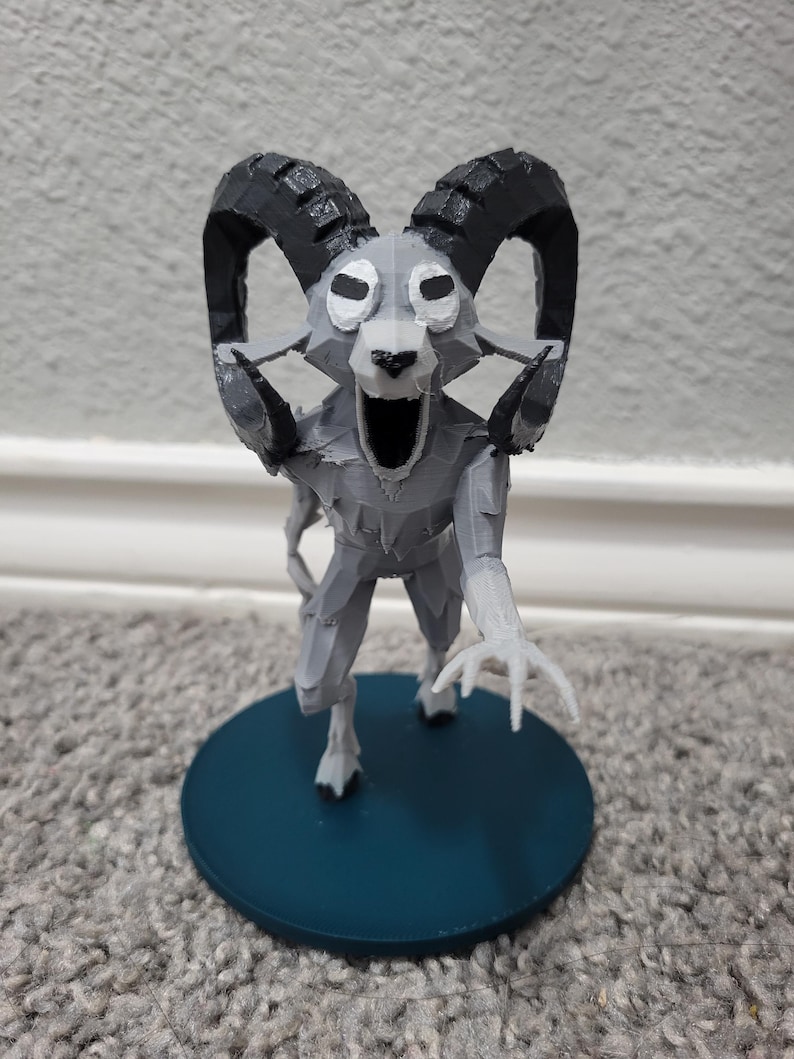 Op de afbeelding: Een 3D-geprinte figuur van een op een ram lijkend wezen met grote gebogen hoorns en een open mond. De figuur is voornamelijk grijs met zwarte hoorns en staat op een cirkelvormige teal-kleurige basis.