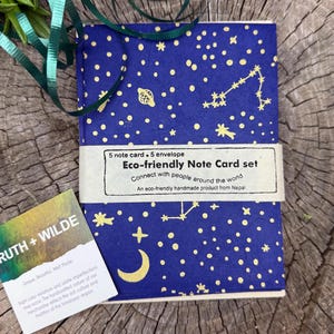 May include: A set of 5 eco-friendly note cards and envelopes with a blue background and gold stars, planets, and constellations. The text on the front reads "Eco-friendly Note Card set. Connect with people around the world. An eco-friendly handmade product from Nepal."