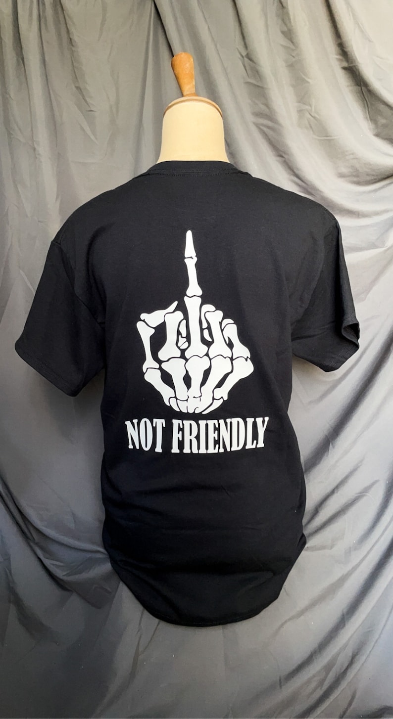 K&ouml;nnte beinhalten: Schwarzes T-Shirt mit einer wei&szlig;en Skeletthand, die den Mittelfinger zeigt, und dem Text "NOT FRIENDLY" auf der R&uuml;ckseite.