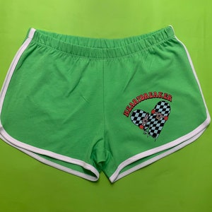 Könnte beinhalten: Grüne Sport Shorts mit weißem Besatz und einem karierten Herz-Motiv, auf dem in roten Buchstaben "Heartbreaker" steht.