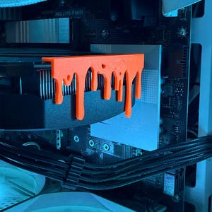 May include: An orange, 3D-printed computer component with a dripping design is mounted on a black heatsink. The component is installed inside a computer case, with other components visible in the background.