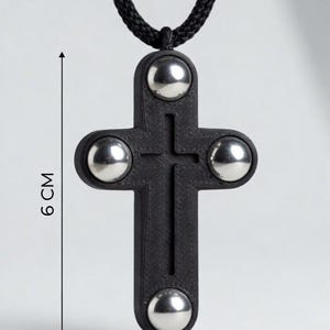 May include: A black pendant necklace featuring a cross design with four silver-colored spheres. The cross measures 3.5 cm wide and 6 cm long, suspended from a black cord.