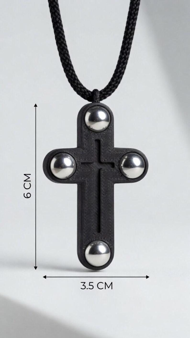 May include: A black pendant necklace featuring a cross design with four silver-colored spheres. The cross measures 3.5 cm wide and 6 cm long, suspended from a black cord.