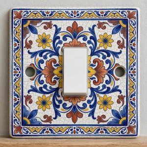 May include: A square light switch cover featuring a white base with a crackled finish and a decorative pattern of blue, yellow, and orange floral and scroll motifs. A single white rectangular rocker switch is centred on the plate.