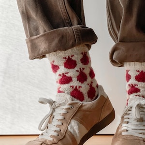 May include: A pair of white socks with red pomegranate designs, worn with brown pants and beige sneakers.