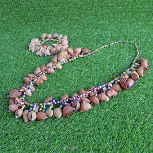 Peut inclure: Un ensemble collier et bracelet avec des pendentifs en graines brunes et des accents de perles colorées. Le collier a une longue chaîne de petites perles multicolores. Le bracelet est une conception circulaire des mêmes graines et perles. Le bijou est posé sur un fond vert.