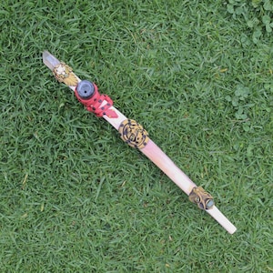 May include: A white wand with a clear crystal at the top and colorful animal figurines attached. The wand is decorated with gold paint and has a green stone at the bottom.