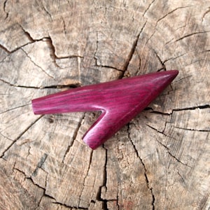 Könnte beinhalten: Ein lilafarbenes Holzkatapult mit einem einzigartigen Design. Das Katapult ist aus Holz mit einer lilafarbenen Beize und liegt auf einem Baumstumpf.