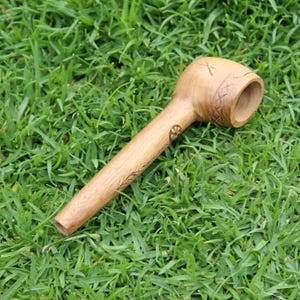 May include: A wooden pipe with a carved design on the bowl and stem. The pipe is lying on a bed of green grass.