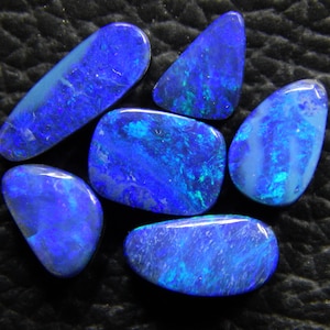 May include: Six blue opal gemstones of various shapes and sizes. The opals have a dark blue base with flashes of green and white.