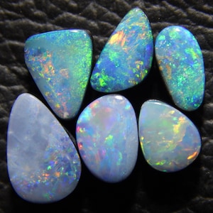 May include: Six iridescent opal gemstones in various shapes and sizes. The opals are a mix of blue, green, and white with flashes of color.