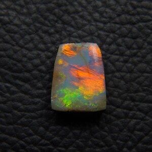 May include: A vibrant, iridescent opal gemstone with a mix of green, orange, and red hues. The opal is cut into a rectangular shape and has a smooth, polished surface.