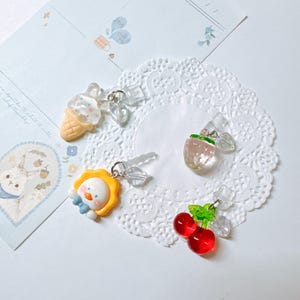 May include: Four colorful charms with clear crystal accents. The charms are shaped like an ice cream cone, a strawberry, a cherry, and a yellow chick.
