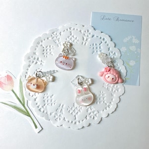 May include: Four pairs of clip-on earrings with cute animal designs: a bear, a cat, a bunny, and a character with a pink bow. The earrings are on a white lace doily with a light blue card that reads "Late Romance".