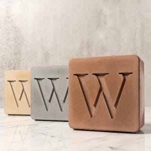 May include: Three concrete blocks with the letter "W" embossed on each. The blocks are in shades of beige, gray, and brown.