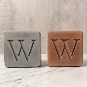 May include: Two concrete letter blocks, one gray and one brown, each with the letter "W" carved into the surface.