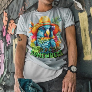 May include: A white t-shirt featuring a colourful parrot wearing a hat and sunglasses. The parrot is holding a green drink. The text on the shirt reads "It's 5 O'Clock Somewhere".