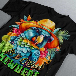 May include: A black t-shirt featuring a colourful parrot wearing sunglasses and a straw hat. The parrot is surrounded by tropical flowers and leaves. The text "It's 5 O'clock Somewhere" is printed on the shirt.