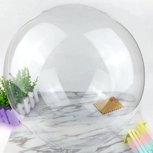 Peut inclure: Un grand ballon rond transparent. Le ballon est gonflé et semble être fait d'un matériau fin et transparent. Le ballon est posé sur une surface en marbre blanc.
