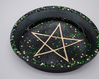 May include: Black circular dish with a gold five-pointed star in the center. The dish is covered in green and gold glitter.