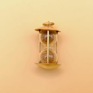 May include: A small, vintage hourglass with a brass-colored frame and end caps. The glass bulbs contain fine, light-brown sand. The hourglass is a classic timekeeping device, often used as a decorative item or for timing activities.