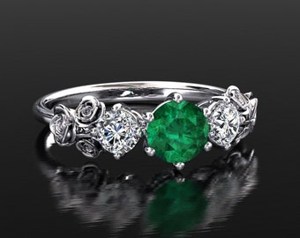 Könnte beinhalten: Ein silberner Ring mit einem grünen Smaragd und zwei kleineren weißen Diamanten, die in einem floralen Design gefasst sind.