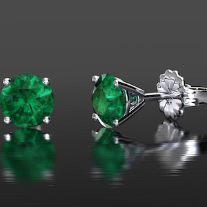 May include: A pair of emerald green gemstone earrings with a silver setting. The earrings are round and have a classic design.