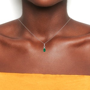 May include: A silver chain necklace with a small emerald green pendant. The pendant is set in a silver frame with small clear stones.