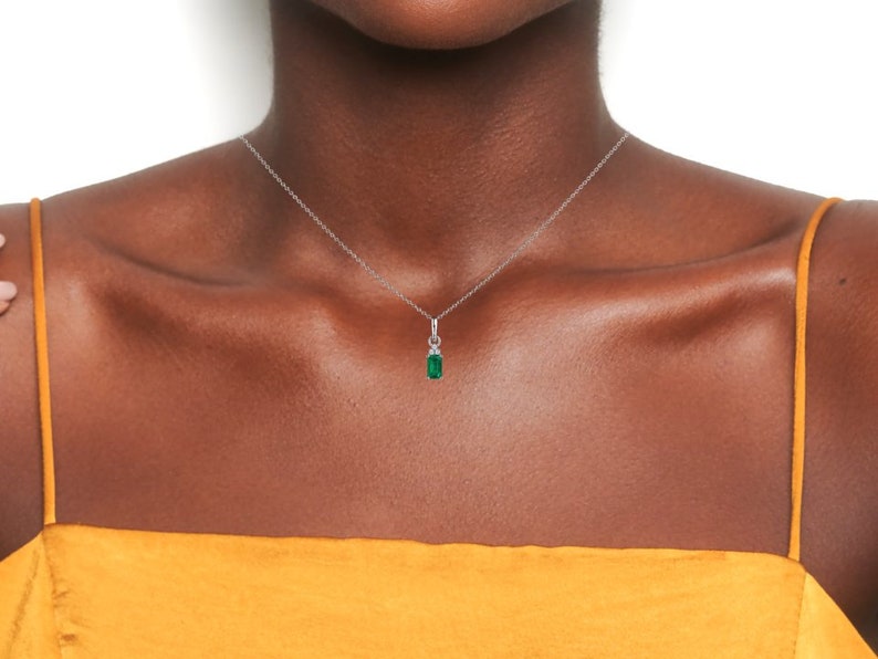 May include: A silver chain necklace with a small emerald green pendant. The pendant is set in a silver frame with small clear stones.