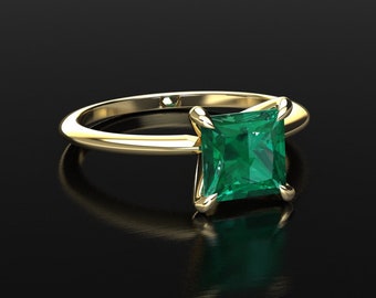 Op de afbeelding: Een gouden ring met een vierkante smaragd edelsteen. De ring heeft een eenvoudige band en de smaragd is gezet in een vier-klauw zetting.