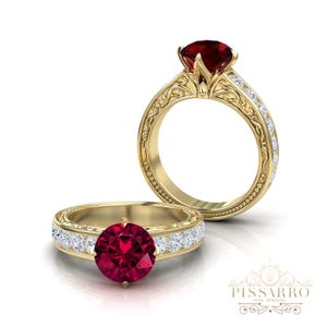 Könnte beinhalten: Zwei goldene Ringe mit einem großen, runden, tiefroten Edelstein. Ein Ring ist fokussiert und zeigt ein detailliertes Filigranmuster auf dem Band und kleine, klare Edelsteine. Der andere Ring ist leicht unscharf. Die Ringe sind vor weißem Hintergrund.