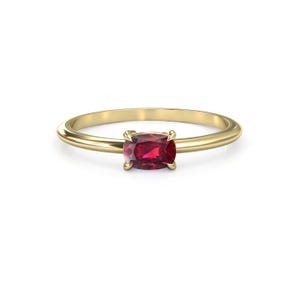 May include: A gold ring featuring a rectangular, deep red gemstone. The ring has a simple, elegant design with a smooth, polished band. The gemstone is securely set in a four-prong setting, showcasing its rich color and brilliance.