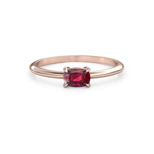 May include: Rose gold ring with a rectangular, deep red gemstone. The thin, polished band holds the gemstone in a four-prong setting. The ring is presented against a white backdrop.