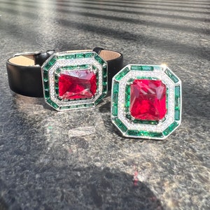 May include: Two large, octagonal-shaped, red gemstone rings with a green and white border. The rings are set on a black leather surface.