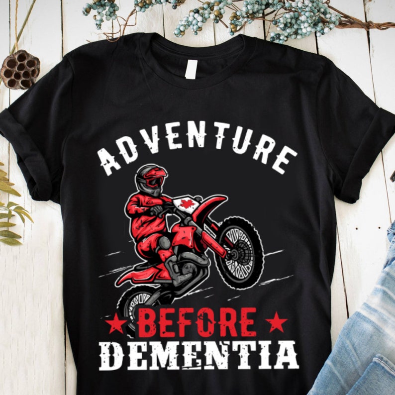 May include: Black t-shirt with a white graphic of a person riding a dirt bike with the text "Adventure Before Dementia" in white.