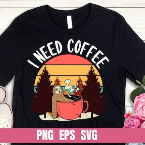 Könnte beinhalten: Schwarzes T-Shirt mit einer Retro-Grafik eines Faultiers, das Kaffee vor einem Sonnenuntergang trinkt. Der Text "I Need Coffee" ist in einem Bogen über dem Faultier geschrieben.