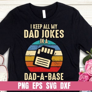 Op de afbeelding: Een zwart T-shirt met een retro-ontwerp met een floppy disk en de tekst "I keep all my dad jokes in a dad-a-base". De tekst is wit en de floppy disk is in een vervaagde rood, geel en blauwe kleurstelling. De onderkant van het shirt heeft de tekst "PNG EPS SVG DXF" in wit.