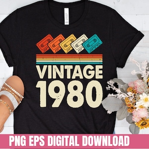 May include: Black t-shirt with a vintage 1980 design featuring a rainbow stripe and cassette tapes. The text "Vintage 1980" is in a retro font.
