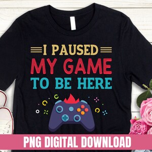 May include: Black t-shirt with a colorful graphic of a video game controller and the text "I paused my game to be here". PNG digital download.