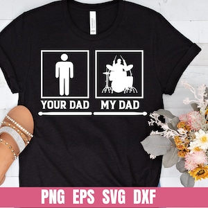 Puede incluir: Camiseta negra con texto blanco que dice "Your Dad" y "My Dad". El lado derecho de la camiseta presenta una silueta de una persona tocando la batería.