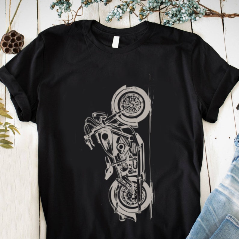 May include: A black t-shirt with a white graphic of a motorcycle on it. The motorcycle is drawn in a stylized way, with the front wheel raised in the air.