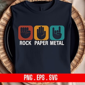 Op de afbeelding: Een donkerblauw T-shirt met drie kleurrijke vierkanten met handgebaren. De vierkanten zijn gelabeld met "Rock", "Papier" en "Metaal".