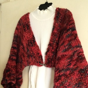 May include: A red, black, and grey knitted cardigan with a V-neck and long sleeves. The cardigan is open in the front and has a loose fit.