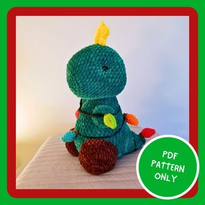 Puede incluir: Un dinosaurio de crochet verde con forma de árbol de Navidad con luces de colores envueltas a su alrededor. El dinosaurio tiene pies marrones y una estrella amarilla en la parte superior de su cabeza. El texto "PDF PATTERN ONLY" está en un círculo blanco en la esquina inferior derecha de la imagen.