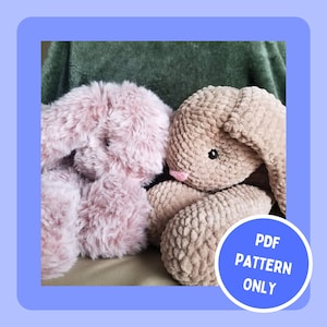 May include: Two crocheted bunny plushies, one in a light pink colour and the other in a light brown colour. The bunnies are sitting next to each other on a green blanket. The text "PDF PATTERN ONLY" is on a blue circle.
