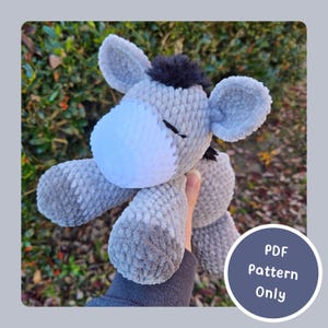 May include: A handmade grey plush donkey toy with a white muzzle and black mane. The donkey has large, floppy ears and is made of soft, textured yarn. The text "PDF Pattern Only" is in a blue circle.
