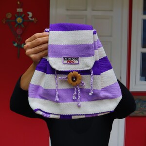 May include: A purple and white striped backpack with a wooden flower button and a label that reads "Tarapoto Peru".