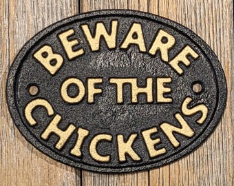 Puede incluir: Un letrero ovalado de hierro fundido negro con las palabras "Beware of the Chickens" en letras doradas.
